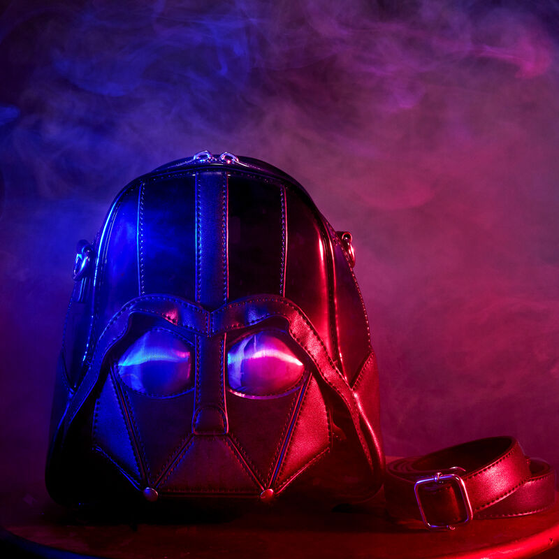 Crossbody bag in the shape of Darth Vader's helmet, against a dark blue and red background with smoke effects around it. 